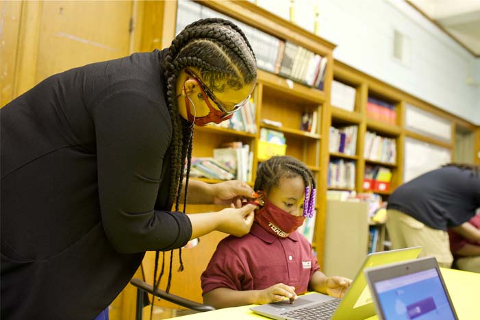 A lady holding a mask of a small boy in class